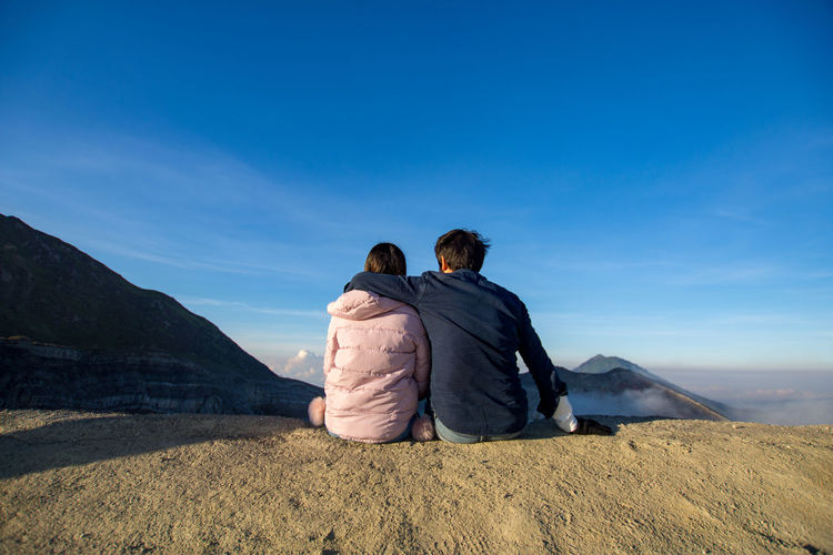 Rear view of couple sitting on land against sky