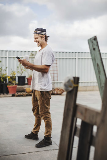 Happy carpenter using mobile phone while standing outside workshop