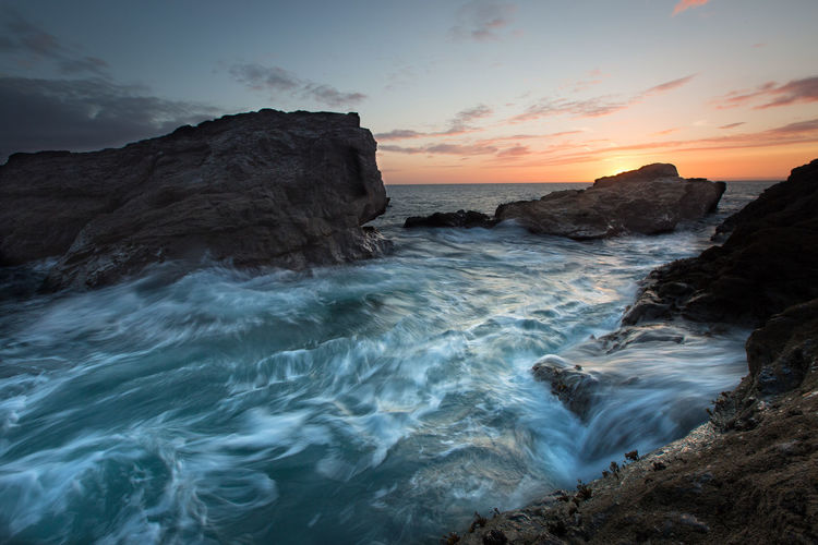 A rugged cornish coastal landscape with crashing waves at sunset with motion blur and dramatic skies