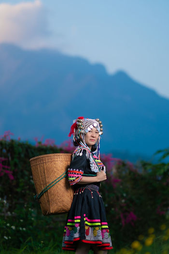 Portrait of smiling woman in traditional clothing holding wicker basket while standing in farm