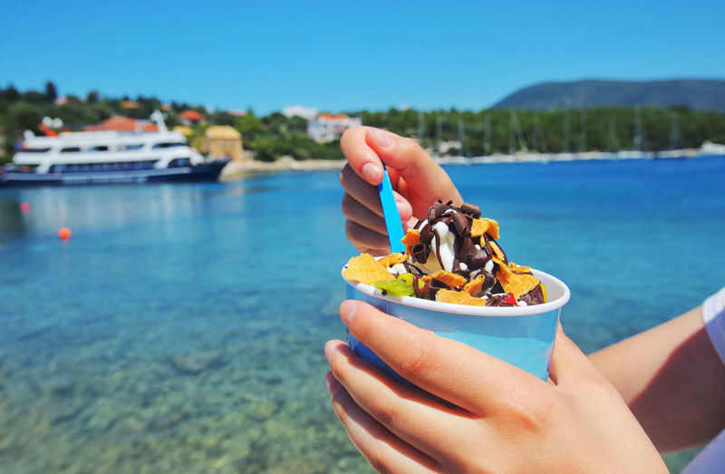 Midsection of woman holding ice cream sundae in container by sea
