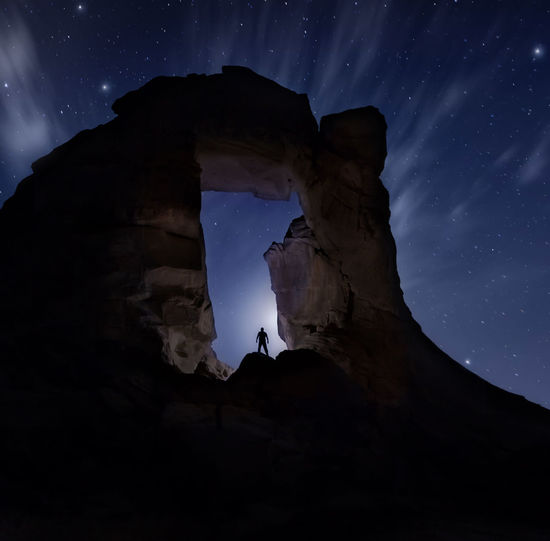 Low angle view of silhouette man standing on rock formation at night