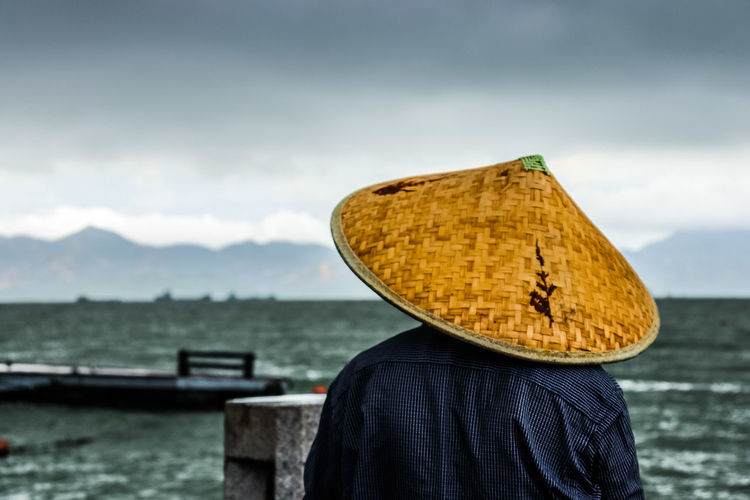 Rear view of men wearing asian style conical hat at beach against sky