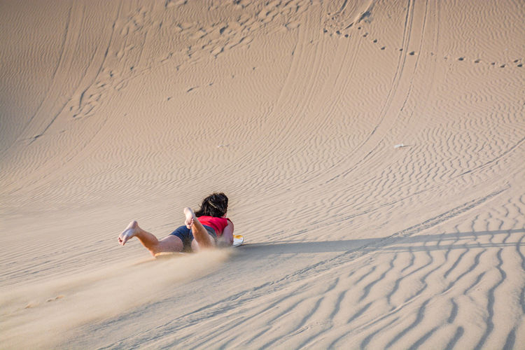 Full length of woman sandboarding in desert