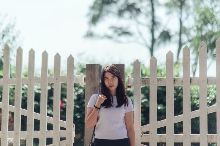 Portrait of young woman standing against fence