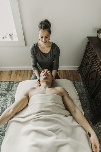 Smiling female massage therapist treats neck of male patient
