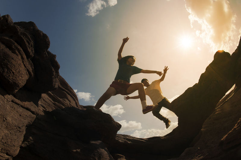 Low angle view of friends jumping over rock formations against sky