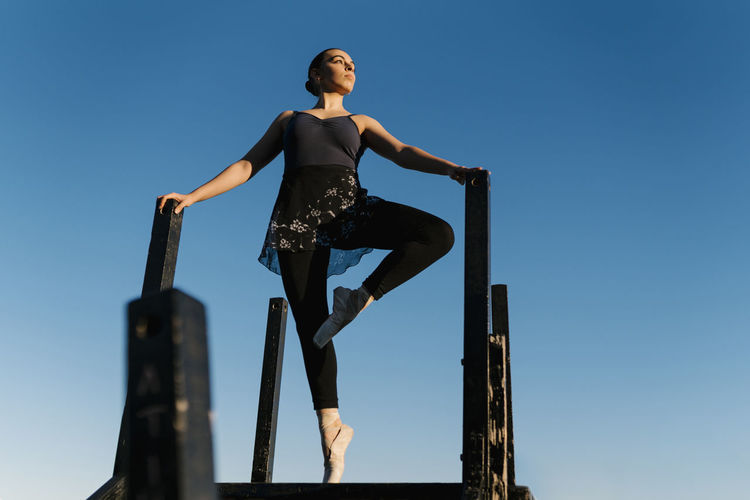 Female ballet dancer looking away while practicing on jetty against sky