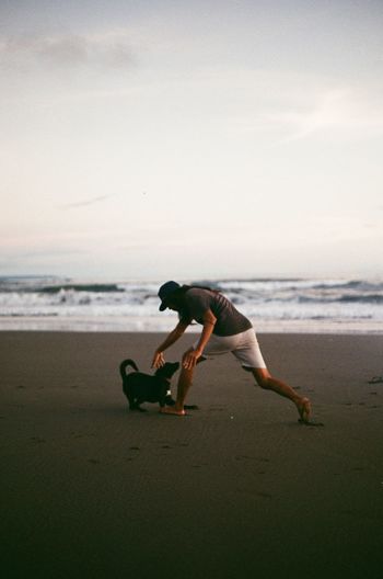 Man playing on sand with the dog at beach against sky