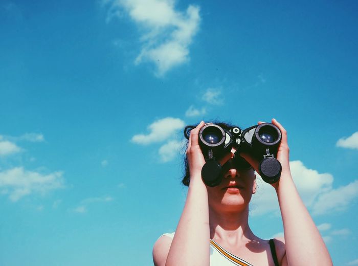 Low angle view of woman looking through binoculars against sky