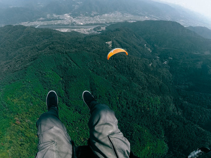 Low section of man paragliding over mountain against sky
