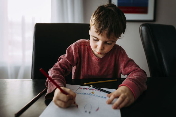 Boy drawing with colored pencil on paper at home