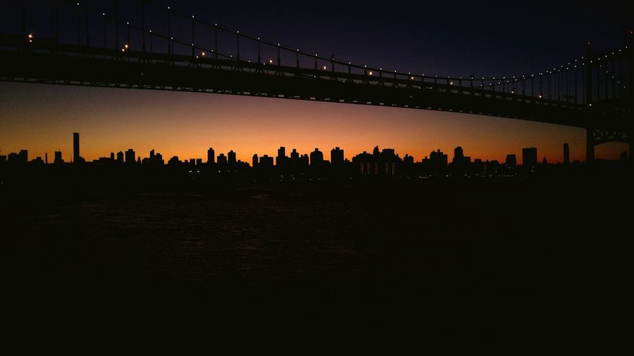 Illuminated silhouette bridge over river against sky at dusk