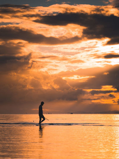 Silhouette man on sea against sky during sunset