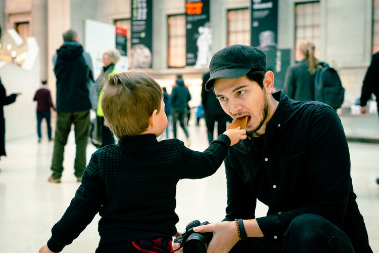 Son feeding food to father in city