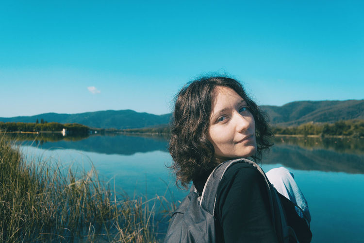 Girl sitting on the edge of banyoles lake on a sunny day with the landscape reflected in the water