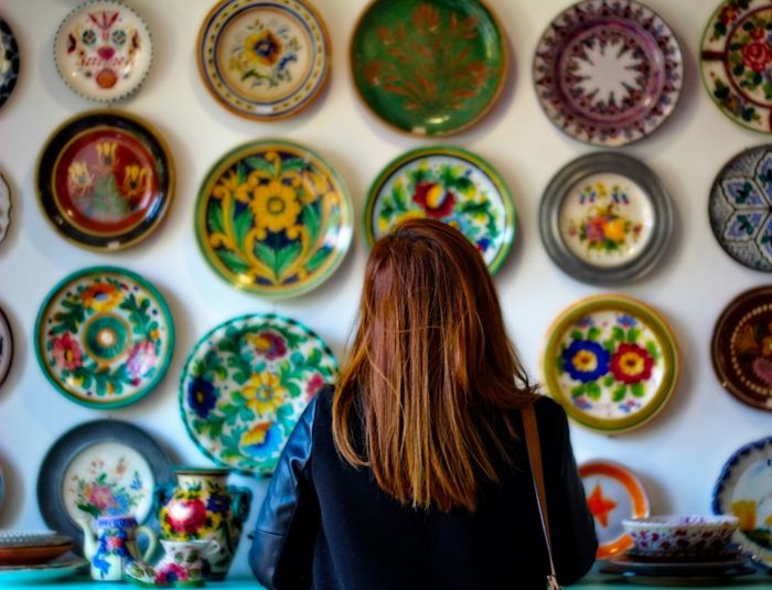 Rear view of woman standing against multi colored dishes on wall