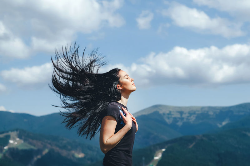 Side view of mid adult woman with eyes closed standing on mountain against cloudy sky
