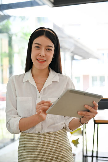 Portrait of smiling young businesswoman using digital tablet while standing in city