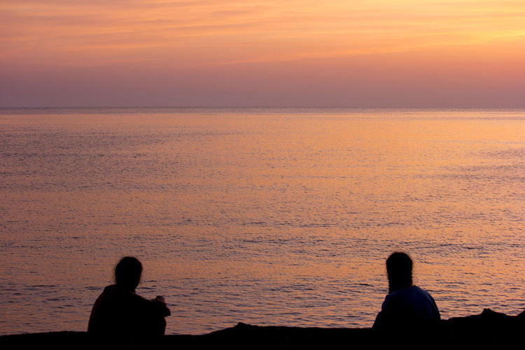 Silhouette men against sea during sunset