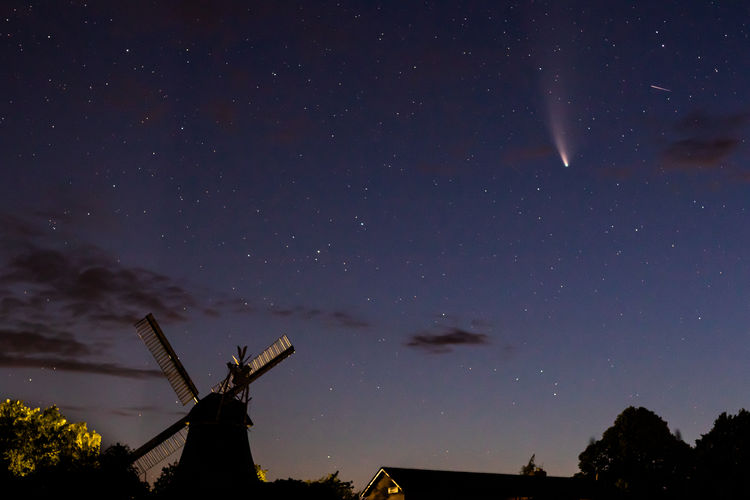 Low angle view of silhouette windmill against sky at night with comet