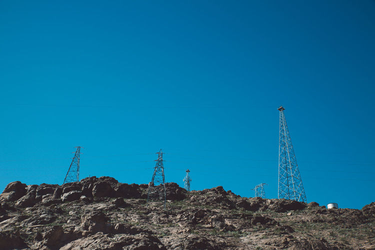 Low angle view of electricity pylons on mountain against clear blue sky