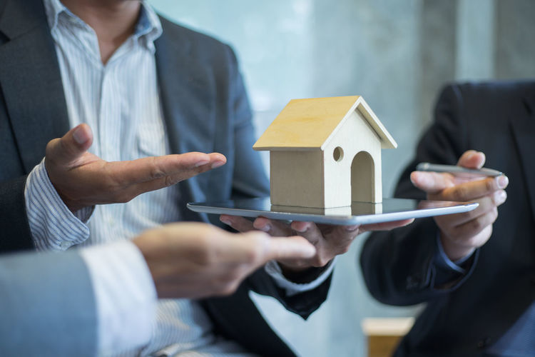 Midsection of businessman holding model house on digital tablet