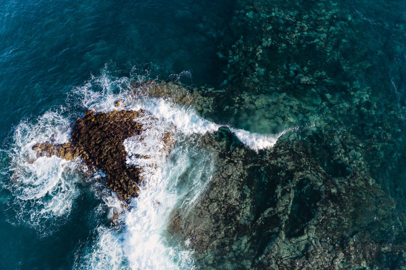 Aerial view of a wave breaking over a sharp lava reef in tenerife.