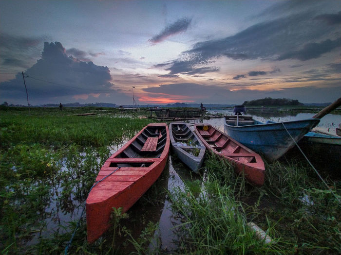 Boats moored on field against sky during sunset