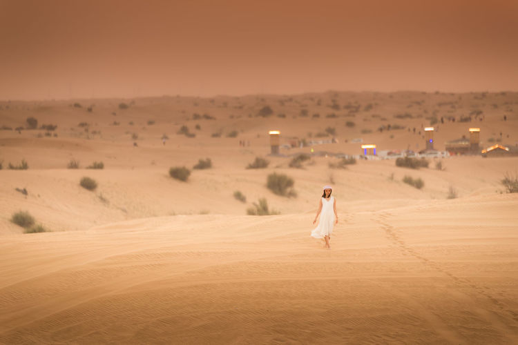 Young woman walking on desert against sky during sunset