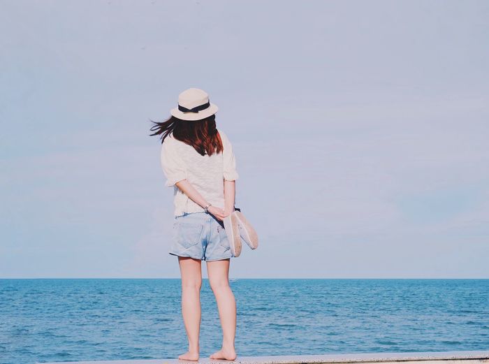 Rear view of young woman standing by sea against sky