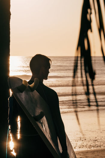 Rear view of young man with surfboard at beach during sunset