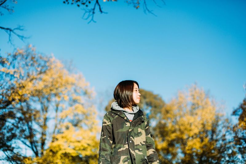 Woman standing by trees against clear sky during autumn