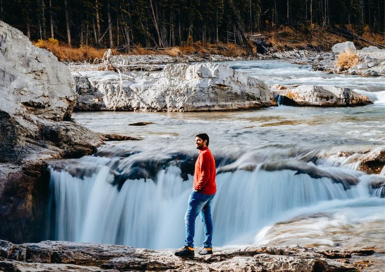 Rear view of man standing on rock against waterfall