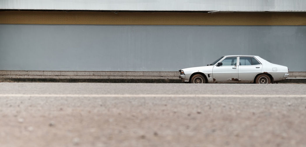An old, broken car parked next to an advertising space and a foreground, blurry road