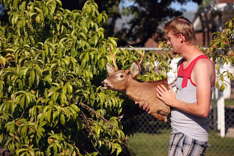 Side view of man holding hunting trophy while standing in yard