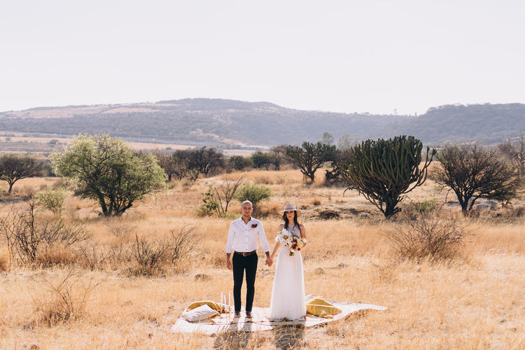 Couple standing on field against clear sky