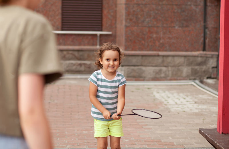 Mother playing tennis with daughter outdoors