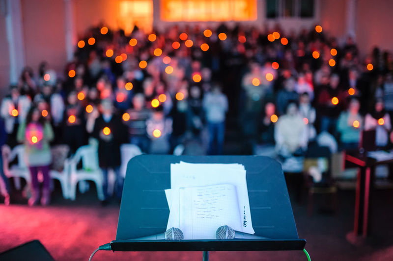 Microphones and sheet music on stand against people at church