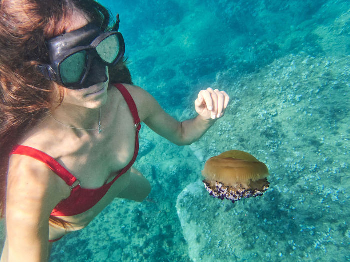 Unrecognizable young woman in diving mask swimming in deep transparent sea water and exploring jellyfish