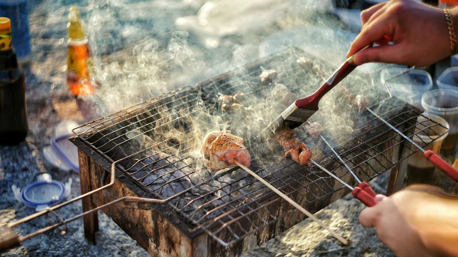 High angle view of hands brushing meat on grill