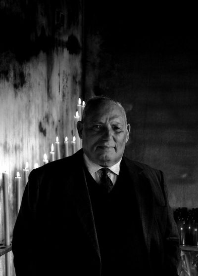 Portrait of man in full suit standing against lit candles