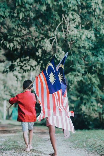 Rear view of people holding malaysian flags against trees