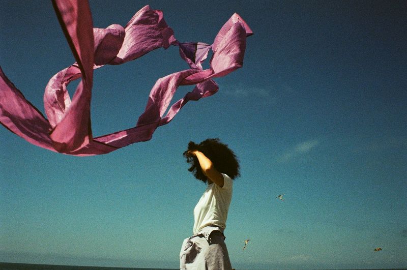 FULL LENGTH OF WOMAN STANDING BY PINK FLOWERS AGAINST SKY
