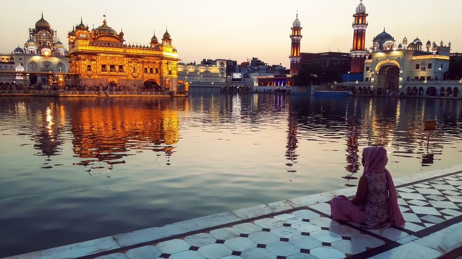 Woman praying by golden temple against sky at dusk