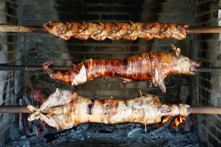 Pork on metallic rod hanging against barbecue