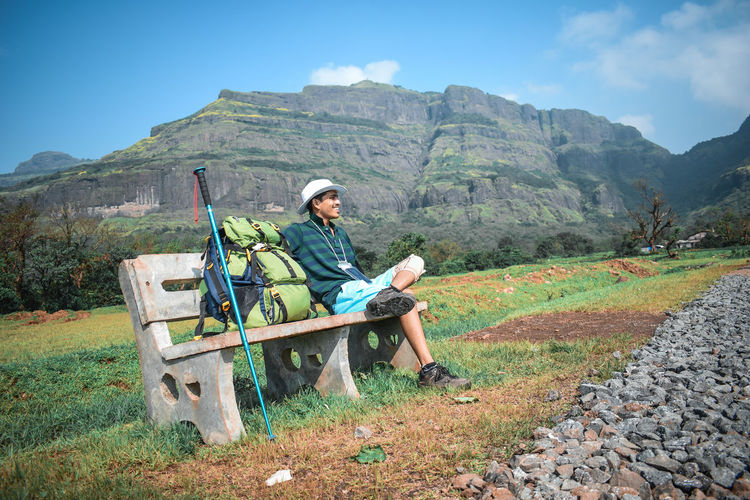 Young man sitting on seat in mountains against sky