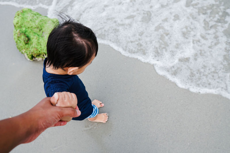 Cropped hand of father holding son hand while standing at beach