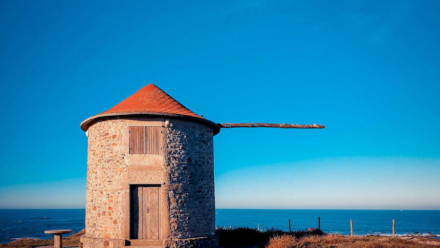 Built structure by sea against clear blue sky