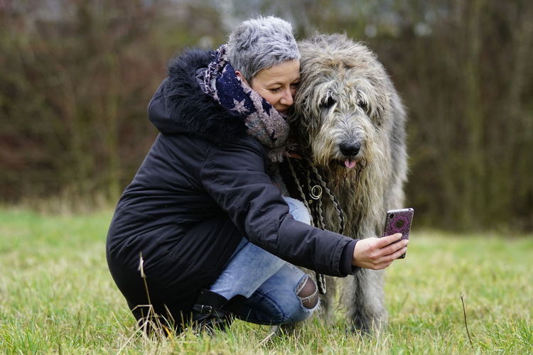 Mature woman with dog taking seflie on grassy field